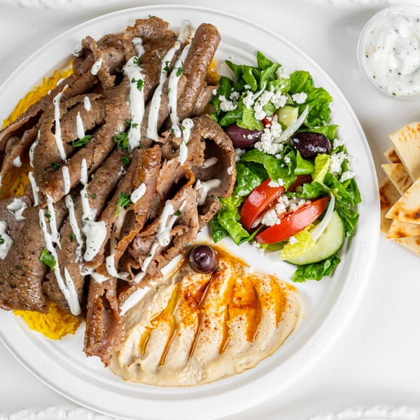 A Greek gyro platter with sliced meat, rice, hummus, a fresh salad, and pita bread.