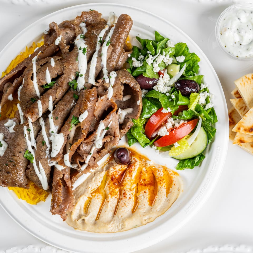 A Greek gyro platter with sliced meat, rice, hummus, a fresh salad, and pita bread.