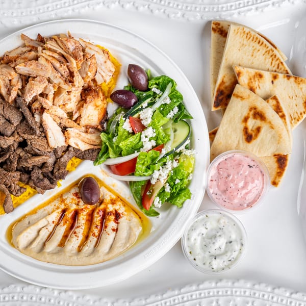 A Greek platter with chicken and beef shawarma, hummus, salad, pita bread, and two dipping sauces.