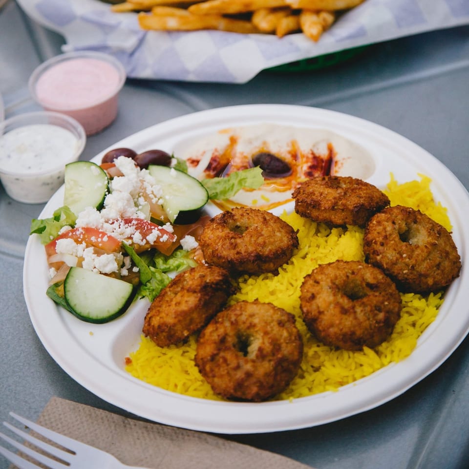 A Greek platter with falafel, yellow rice, hummus, Greek salad, and dipping sauces.