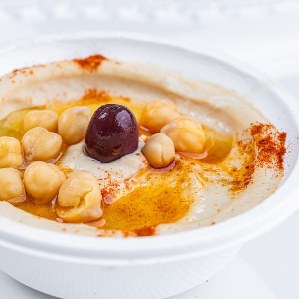 Creamy hummus with chickpeas, a black olive, olive oil, and paprika in a white bowl.
