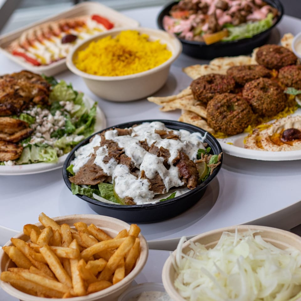 A table filled with various Greek dishes including gyros, falafel, rice, salads, and fries.