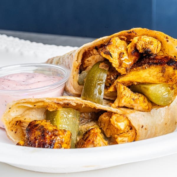A chicken shawarma wrap with pickles and a side of pink sauce on a white plate.