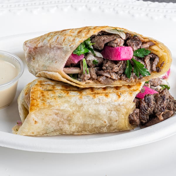 Two Greek shawarma wraps, one cut in half, filled with meat, pickled turnips, and parsley.
