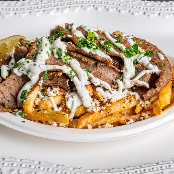 A Greek gyro plate with sliced meat, french fries, feta cheese, and tzatziki sauce.
