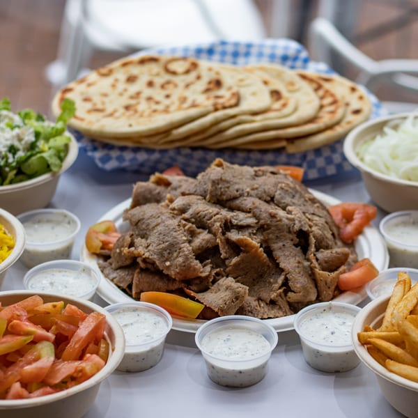 A Greek gyro platter with sliced meat, pita bread, salad, fries, tomatoes, onions, and tzatziki sauce.