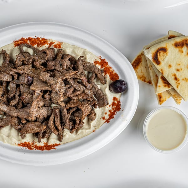 It's All Greek To Me's beef shawarma over hummus, with pita bread and tahini sauce.