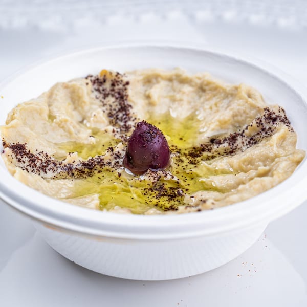 Creamy hummus with olive oil, sumac, and a single dark olive in a white bowl.