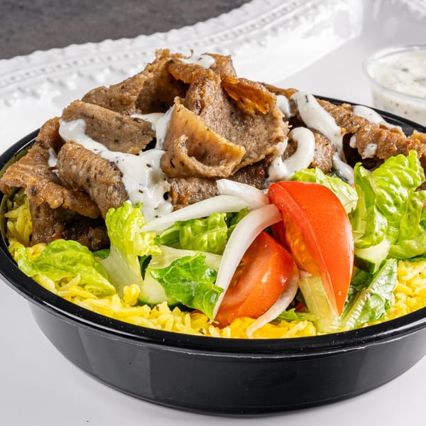 A Greek gyro bowl with sliced meat, rice, lettuce, tomatoes, onions, and tzatziki sauce.