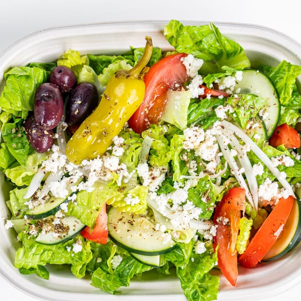A vibrant Greek salad with lettuce, tomatoes, cucumbers, olives, feta, and a pepperoncini.