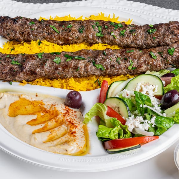 Two Greek beef kebabs on yellow rice, with hummus, salad, and an olive.